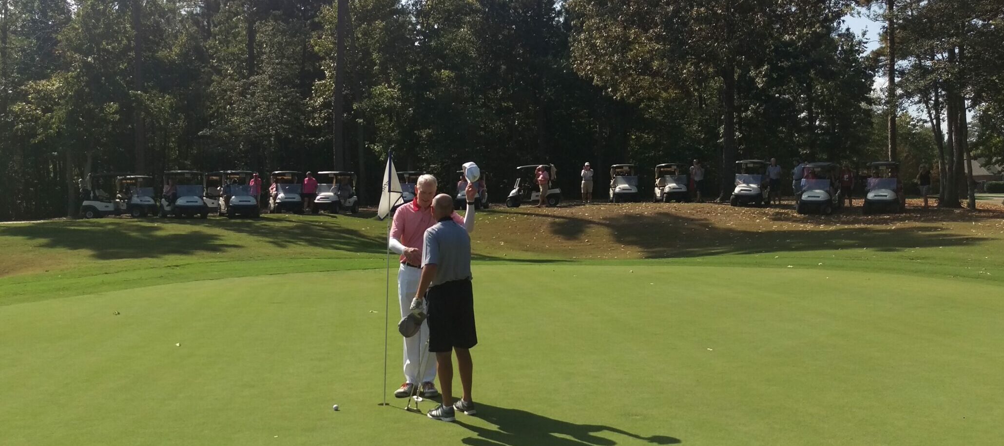 two men near hole on golf course at Williamsburg National Golf Club with golf carts in the background